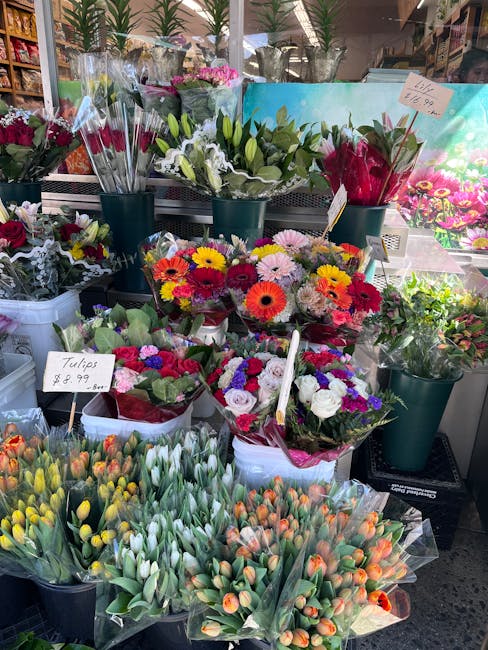 A vibrant floral display at a flower shop featuring a variety of fresh bouquets and arrangements. In the foreground, there are multiple bundles of tulips with closed buds in shades of yellow, white, a