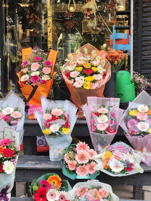 A vibrant display of fresh flower bouquets arranged on a black wooden table outside the flower shop, showcasing a variety of floral arrangements. The bouquets include pink, white, yellow, and red dais